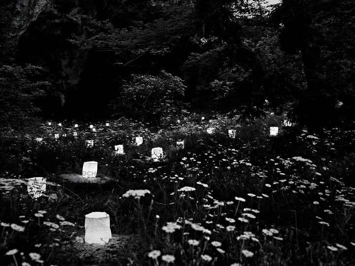 Christmas lanterns at dusk in meadow by cave - AI-generated stock image