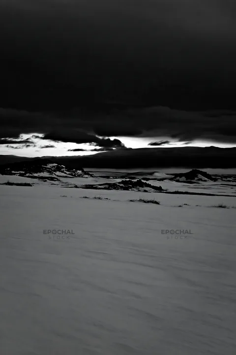 Snowbound meadow under dark clouds at twilight - AI-generated stock image