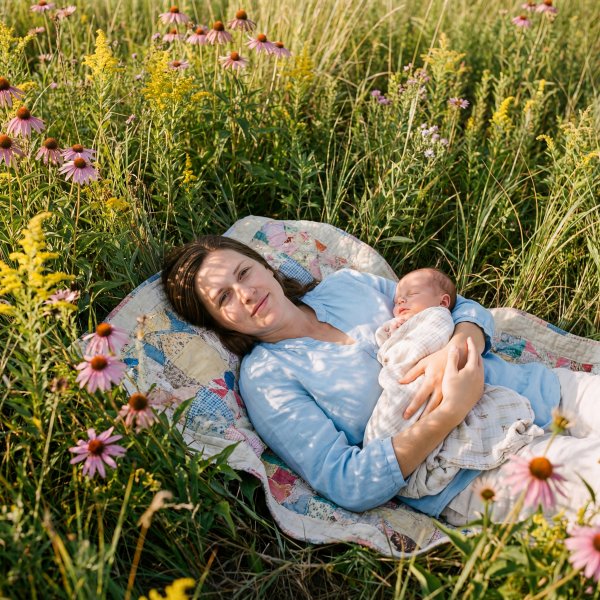 Mother rests in a field with her newborn baby during daytime - stock photo