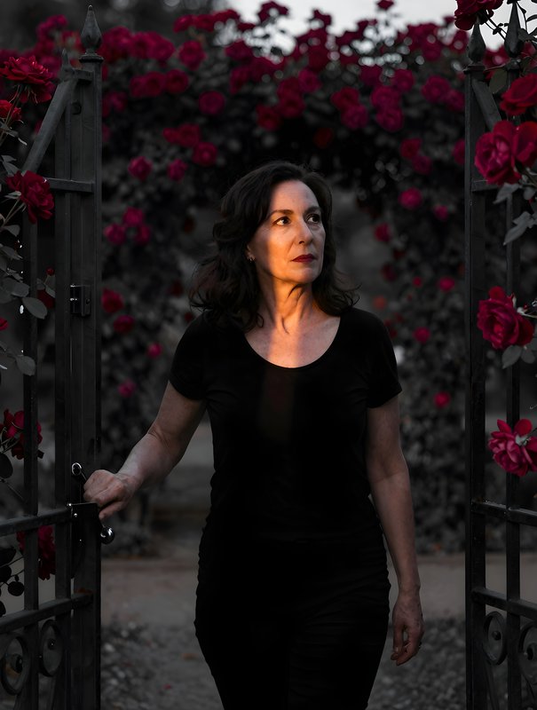 Woman walks through a gate with roses in the background Premium Stock Image - stock photo