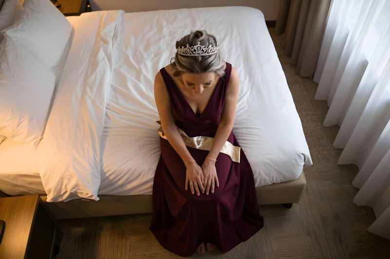 Woman in gown sitting on bed with crown Premium Stock Image - stock photo