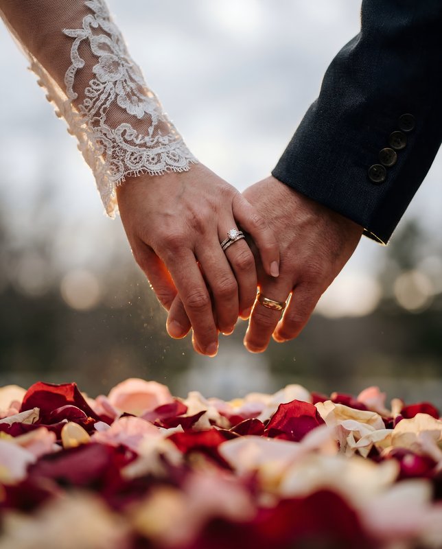 Couple holds hands surrounded by rose petals in outdoor space Premium Stock Photo - stock photo