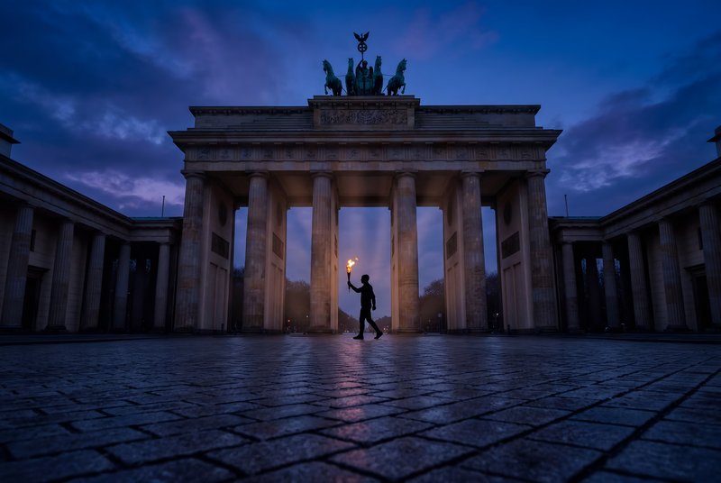 Person walks with torch near Brandenburg Gate at dusk Premium Stock Image - stock photo