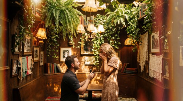 Man proposes to woman in cozy room with warm lighting and plants - stock photo