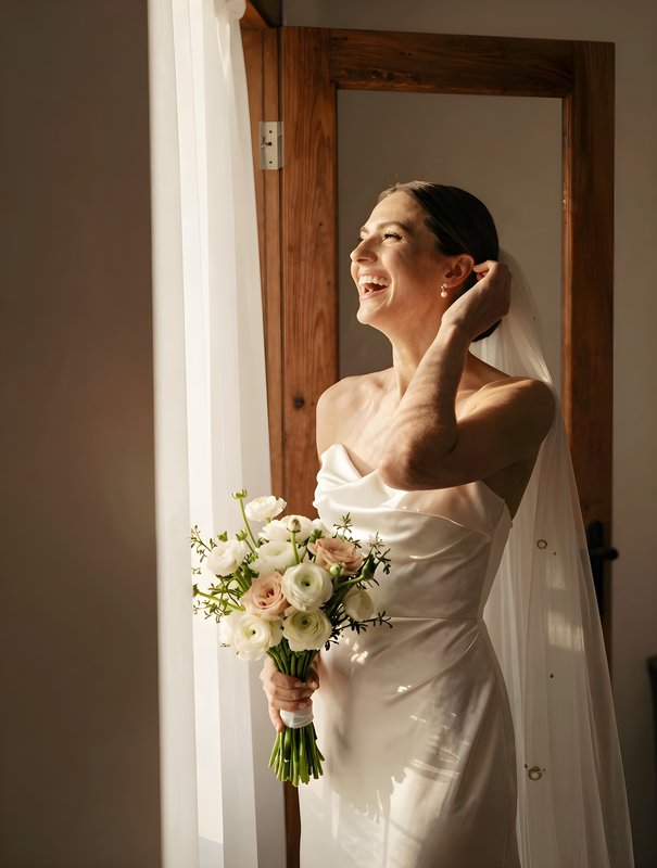 Bride smiles by the window with bouquet before the ceremony Premium Stock Photo - stock photo