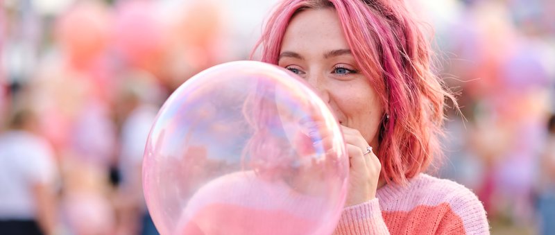Woman blows pink bubble in outdoor festival setting Premium Stock Photo - stock photo