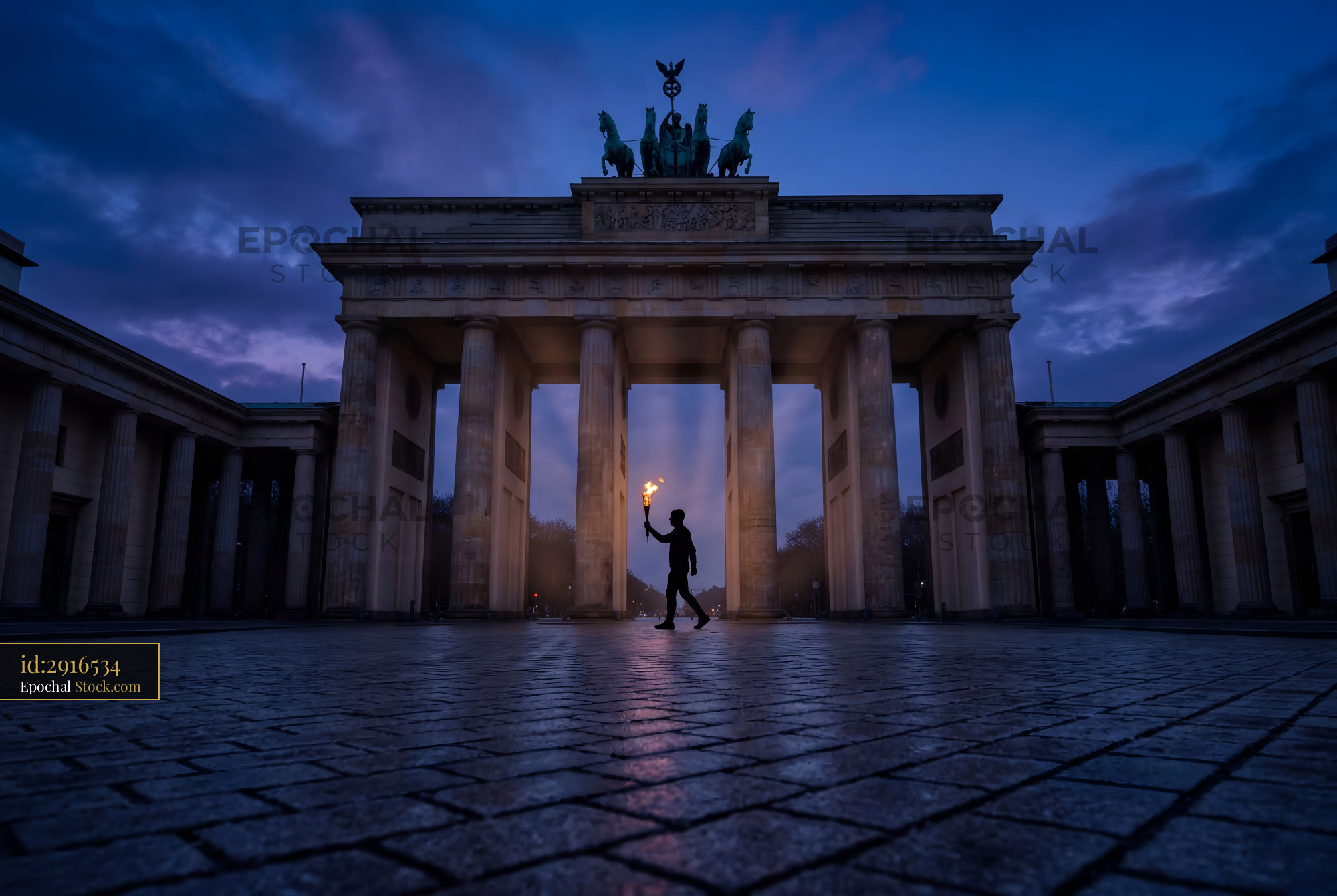 Person walks with torch near Brandenburg Gate at dusk Premium Stock Image